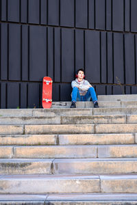 Teenager with headphones listening music while sitting on staircase.