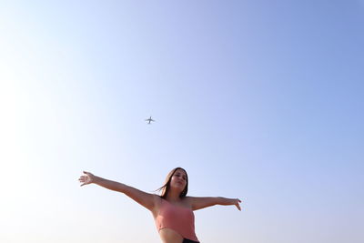 Low angle view of woman flying airplane against clear sky