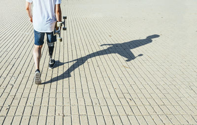 Young man with leg prosthesis walking and holding skateboard