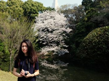 Portrait of beautiful young woman standing on rock against trees