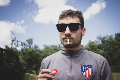 Portrait of young man wearing sunglasses standing against sky