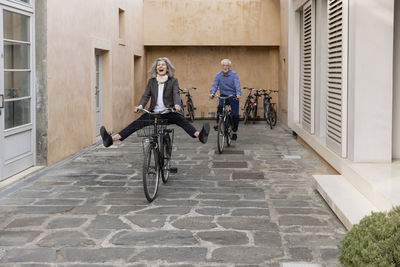 Happy senior woman riding bicycle with man on footpath