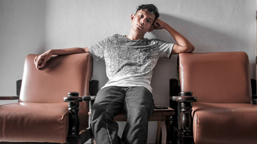 Portrait of man sitting on table amidst chairs at home