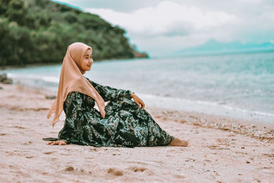 Woman sitting on beach by sea against sky