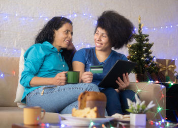 Smiling mother and daughter holding coffee cup while video conferencing over tablet