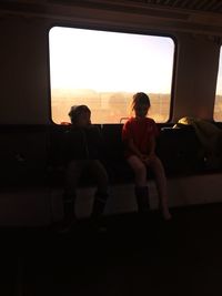 Boy sitting on window at sunset