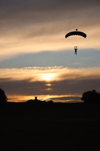 Silhouette person paragliding against sky during sunset