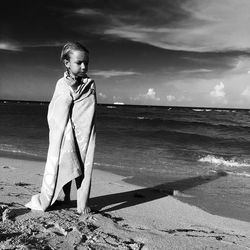 Full length of girl covered with towel at beach against sky