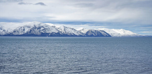 Idyllic view of seascape and snowcapped mountains against cloudy sky