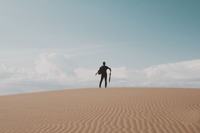Rear view of man holding umbrella on desert against sky