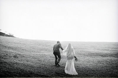 Newly married couple on field against clear sky