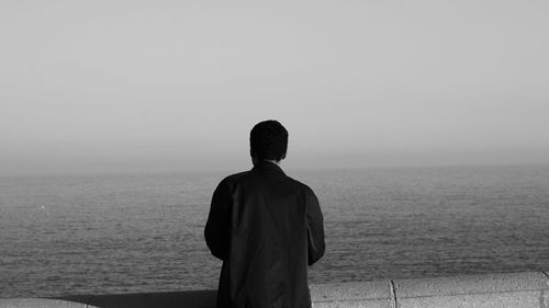 Rear view of man standing at beach against clear sky