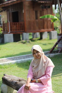 A muslim woman is sitting smiling in a park, with a blurred background.