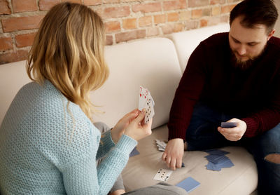 Couple playing cards while sitting on sofa at home