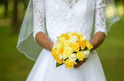 Midsection of bride holding yellow roses bouquet