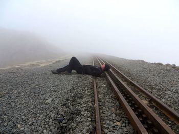 Full length of man resting on railroad track during foggy weather