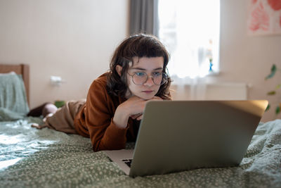 Interested teen girl spending weekend, pastime at home, watching video, film on laptop computer