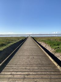 Wooden walkway leading out to the sea with a blue sky background 