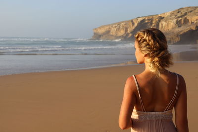 Rear view of woman standing at beach against sky