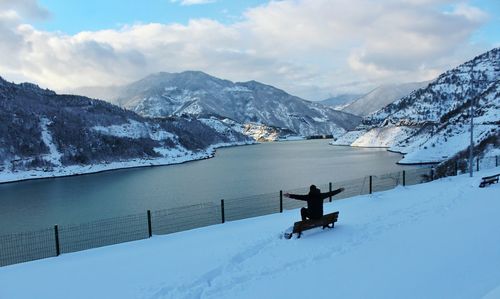 High angle view of man sitting with arms outstretched on bench during winter