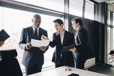 Young businessman discussing with senior adult while colleague walking away in conference room at office