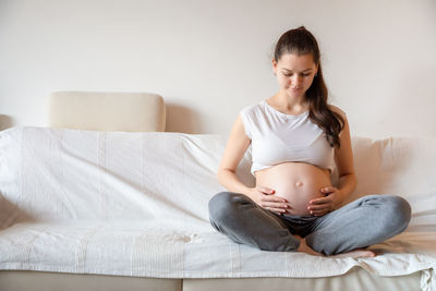 Young pregnant woman holding stomach sitting on sofa at home