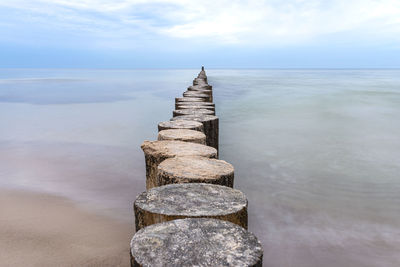 Wooden breakwater covered with moss, arranged in a row at sea, long exposure time, blurred sea waves