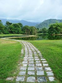Footpath amidst trees on field against sky