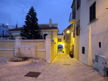 Illuminated alley amidst buildings against sky