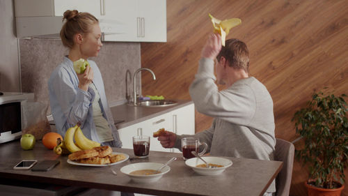 Man throwing banana while talking with wife at kitchen