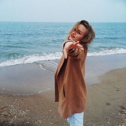 Young woman standing at beach against sky