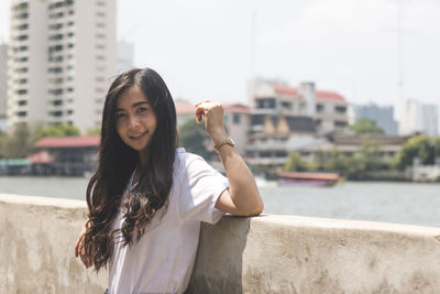 Portrait of smiling young woman by retaining wall in city