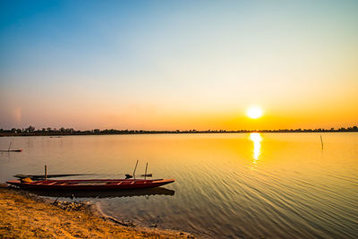 Sailboats moored in lake against sky during sunset