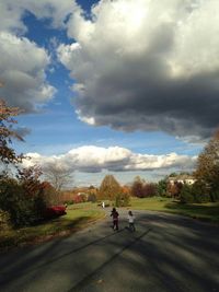 People walking on road against cloudy sky