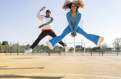 Confident male and female friends jumping while dancing on basketball court