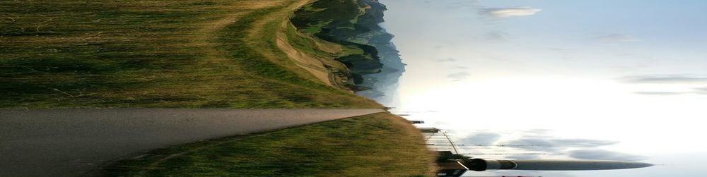 Scenic view of field by sea against sky