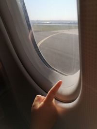 Cropped image of hand pointing by window in airplane