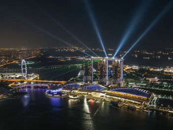 Illuminated city by river against sky at night