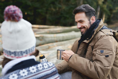 Close-up of smiling man holding cup sitting outdoors