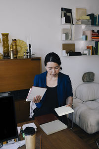 Mature female architect holding diary while standing at desk in home office