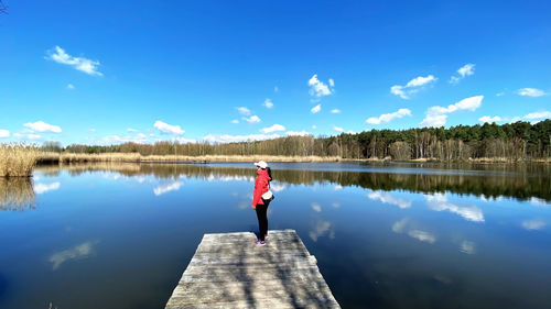 Man standing on pier over lake against blue sky