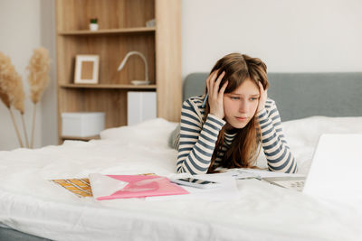 Portrait of young woman sitting on bed at home