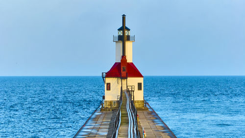 Lighthouse by sea against clear sky