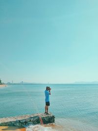 Full length of man photographing while standing on pier against sky