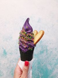 Cropped hand of woman holding ice cream against wall