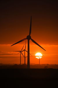 Silhouette windmill on field against orange sky