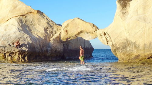 Man standing on rock by sea against sky