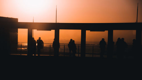 Silhouette people standing against orange sky during sunset