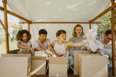 Group of multiracial volunteers sorting donation goods in boxes under tent at community center