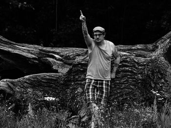 Hipster with hand raised while standing against log in forest